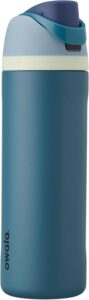 An Owala FreeSip Insulated Stainless Steel Water Bottle in the color 'Shy Marshmallow.' The bottle is shown standing upright on a clean, light-colored surface, highlighting its unique two-in-one lid with both a built-in straw and a wide-mouth opening. The image focuses on the bottle's sleek design, showcasing its BPA-free, leakproof construction, and the secure carrying loop. The bottle is a perfect compan